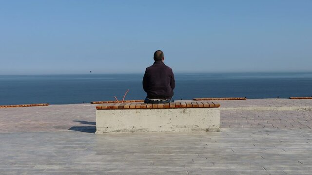 One man sits alone in front of the sea view. Man sitting on the bench by the sea facing the sea. Loneliness and thinking people concept