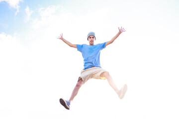 Fototapeta na wymiar Young man jumping and celebrating with his arms raised and the sky in the background. Man jumping for joy and feeling happy and free. Success and happiness concept.
