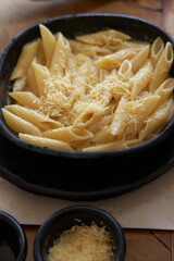 Close-up of a grass penne pasta with Parmesan cheese served in a black clay bowl.  