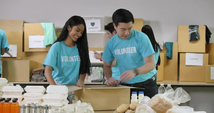 Young asian male and female volunteer preparing free food delivery in a donation grocery box together as charity workers and members of the community work to the poor during the Coronavirus pandemic.