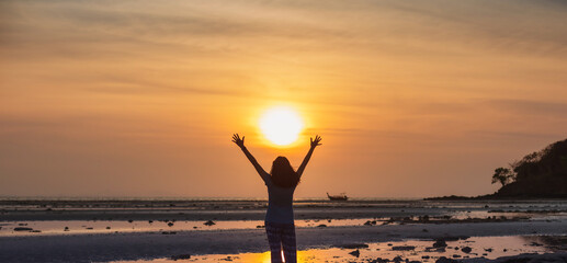 Fototapeta premium Asian woman standing on the beach by the sea at morning sky with sunrise background.