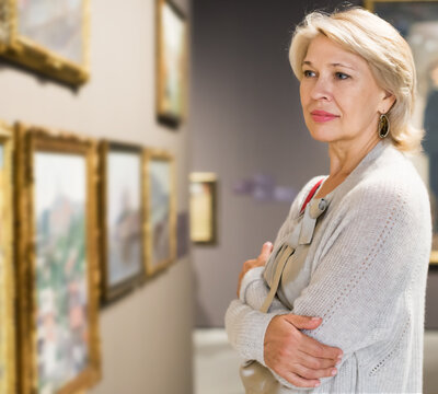 Portrait of positive adult woman near picture collection in the museum
