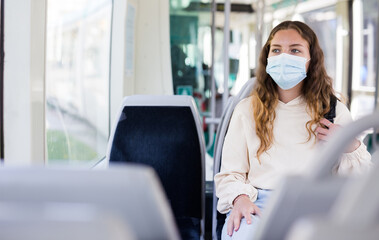 Young attractive lady in protective face mask riding on tram to her work - obrazy, fototapety, plakaty
