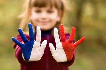 Joyful girl waving hands painted in France flag colors and say hello outdoor at sunset background