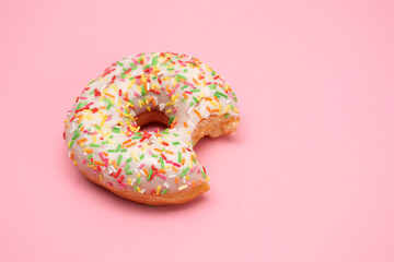 Fototapeta na wymiar Donut with colorful sprinkles on pink background. Pink frosted donut with colorful sprinkles.