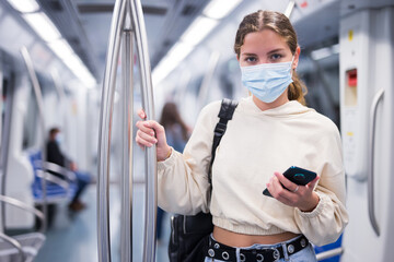 Fototapeta na wymiar Young stylish woman in a protective face mask with mobile phone traveling by train on subway
