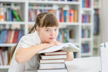 Thoughtful girl with syndrome down reads a book at library. Education for disabled children concept