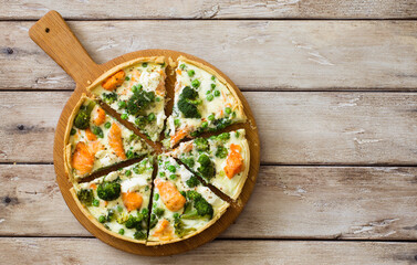 Homemade pie (quiche) with salmon and broccoli on wooden table