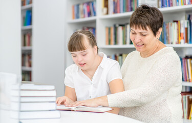 Happy senior teacher and girl with syndrome down read a book at library. Education for disabled children concept