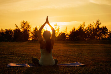 Concept of healthy lifestyle and relaxation-back view of attractive girl in sportswear sitting in lotus position while doing yoga outdoor on sunset