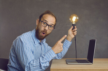 Portrait of funny surprised nerdy bearded man in geek eyeglasses sitting at office desk with laptop...