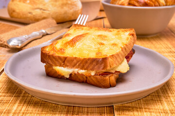 french grilled cheese sandwich (croque monsieur) on a brown plate on a wooden table accompanied by...