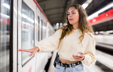 Confident girl with a backpack, who is standing on the platform of a subway station, is about to enter a train car