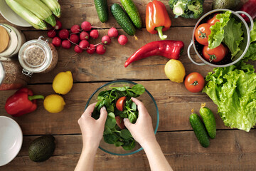 Female hands preparing fresh salad. Set of fresh vegetables for cooking healthy summer food on wooden background top view