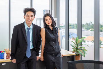 Asian businessman and businesswoman discussing with computer at desk, working together at workplace office, looking at camera.