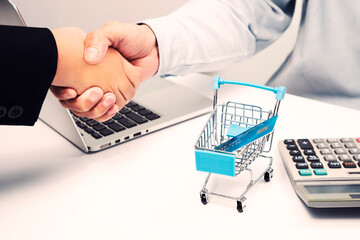 Close up, Businesspeople two shaking hands with credit card in shopping cart, laptop, calculator on white desk in office