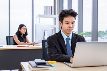 Young Asian man sitting at office desk and working with laptop computer. Businessman or salary man life.