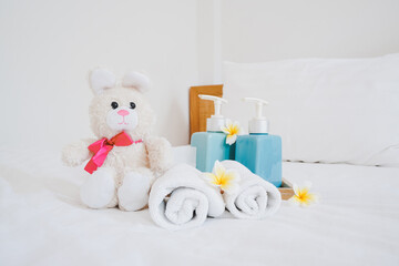 cute rabbit doll and bath room accessories, blurred towels on white cleaned comfortable bed for recreation or summer and holiday concept