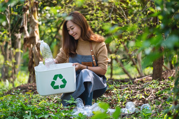 A beautiful young asian woman collecting and putting plastic bottles into a recycle bin in the...