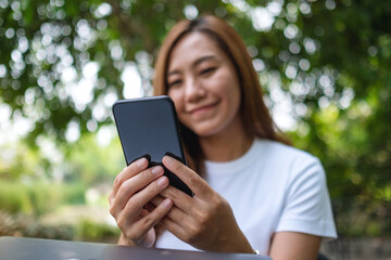 A beautiful young asian woman holding and using mobile phone in the park