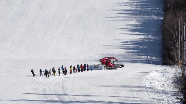 Red snow groomer turning right towing a group of skiers,snowy hill.