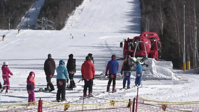 Red snow groomer towing a group of skiers towards a ski slope,Czechia.