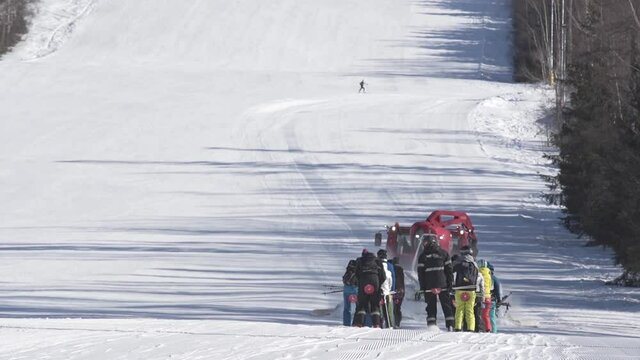 Red snow groomer towing a group of skiers uphill a ski slope,Czechia.