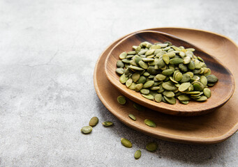 Wooden plate with pumpkin seeds on a gray concrete background