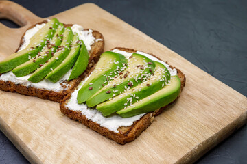 Sandwich with avocado and cottage cheese. Sliced avocado on toasted bread for healthy breakfast or snack. Wholesome food on a plate on the kitchen table. Toasted cereal bread toast. Useful diet food.