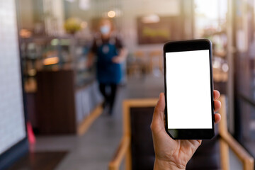 Hand man holding black mobile phone with blank white screen with blur coffee shop background. Mockup image of hand holding smartphone with blank white screen with copy space