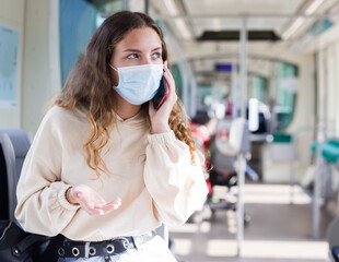 Girl in a protective mask, riding on public transport during the pandemic, communicates on a mobile phone, diskussing..current topics