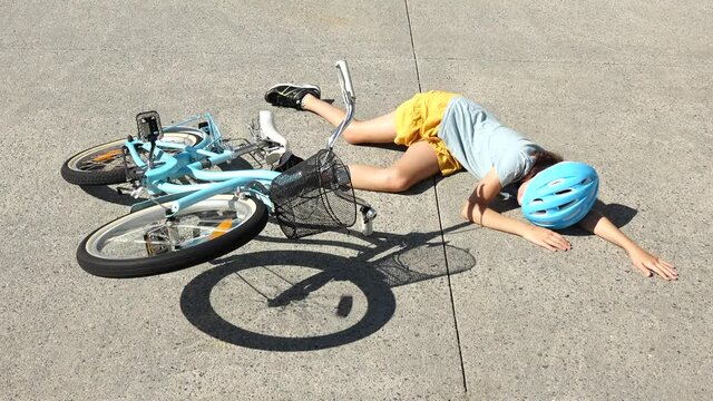Young girl (female age 10-11) fallen of a bicycle laying down beside her bike unconscious on paved road. Above view. Real people. Copy space
