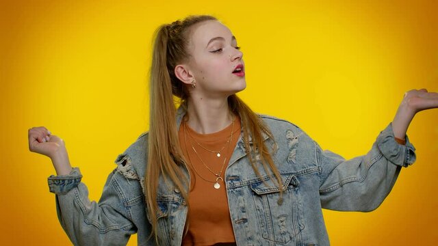 Smiling romantic pretty stylish teen girl in denim jacket sending lots of air kisses looking at camera and smiling, missing you, love confession. Young woman. Indoor studio shot on yellow background
