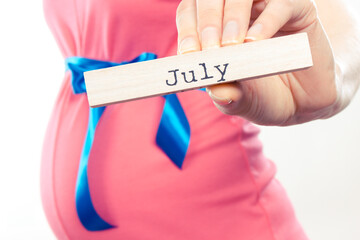 Pregnant woman in pink dress with blue ribbon showing word july. Expecting for newborn and expansion of family