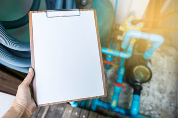 Blank A4 paper sheet on wooden clipboard over blurred swimming pool piping and filtration system, maintenance service, engineering report
