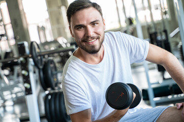 Naklejka na ściany i meble Sport man lifting up dumbbell sitting in private sport gym