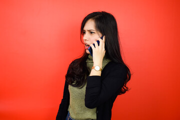 Angry over the phone of Young beautiful asian women using black sweater with red isolated background