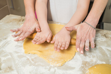 Hands of mom and son who roll out the dough in the kitchen. Cooking at home