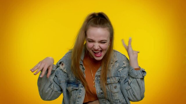 Little bit crazy. Teen stylish girl in denim jacket demonstrating tongue out, fooling around, making silly faces, madness. Young woman posing isolated on yellow studio wall background. Slow motion