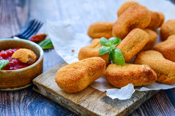 
 Crispy oven baked  chicken nuggets and ketchup. Breaded chicken fillets  with chilly peppers and fresh basi on wooden rustic background