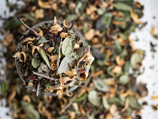Organic herbal tea in a glass jar with dried herbs scattered around on a white background in the morning light