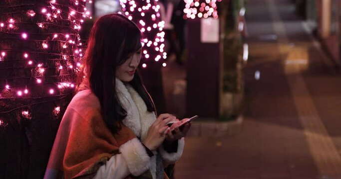 A Japanese woman sending message at the illuminated street closeup