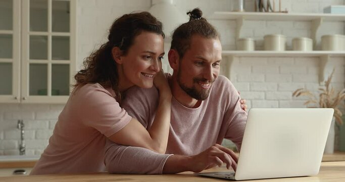 Emotional loving sincere young couple looking at computer screen, celebrating getting last-minute travel tour or getting online lottery giveaway betting auction notification, feeling happy indoors.