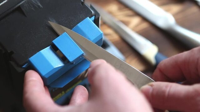 Sharpening a knife on an electric sharpener at home. The man's hand drives the knife blade between the blue sharpeners, dust flies on the machine. Kaluga, Russia, April 25, 2021
