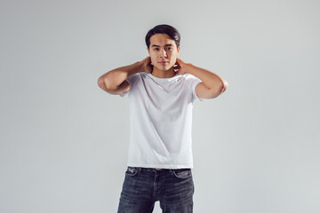 Attractive asian man in white t-shirt stands on white background.