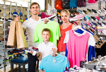 positive spanish couple with boy choosing shoes in sport shop