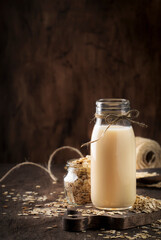 Vegan oat flakes milk, non dairy alternative milk in glass, wooden rustic table, copy space