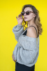Positive woman wearing warm grey knitted winter sweater isolated on yellow wall.