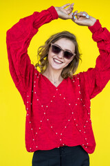 beautiful smiling girl in glasses wearing a red knitted sweater  near the yellow wall