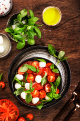 Summer italian salad Caprese with red tomatoes and mozzarella cheese with green basil leaves and olive oil dressing. Top view, wooden table